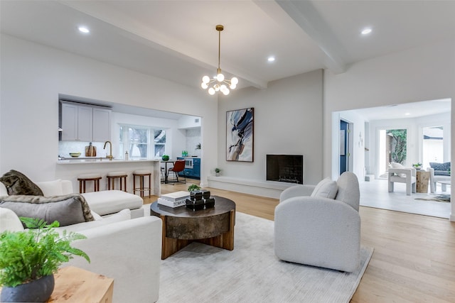 living room with beam ceiling, recessed lighting, a fireplace with raised hearth, an inviting chandelier, and light wood-style floors