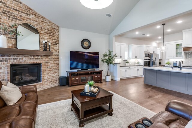 living room with high vaulted ceiling, light wood-style flooring, recessed lighting, a fireplace, and visible vents