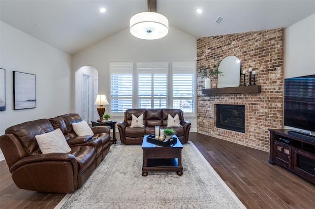 living area featuring arched walkways, a fireplace, wood finished floors, and visible vents