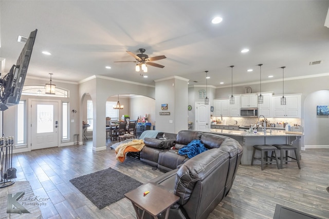 living area featuring arched walkways, dark wood finished floors, visible vents, and crown molding