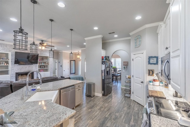 kitchen with arched walkways, a kitchen island with sink, a fireplace, open floor plan, and appliances with stainless steel finishes