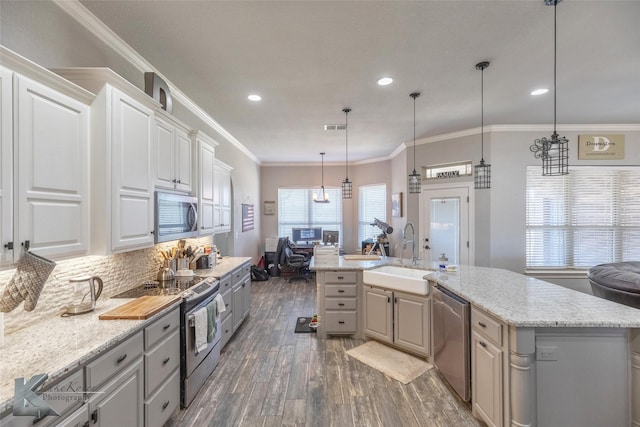 kitchen with light stone counters, open floor plan, appliances with stainless steel finishes, a center island with sink, and pendant lighting