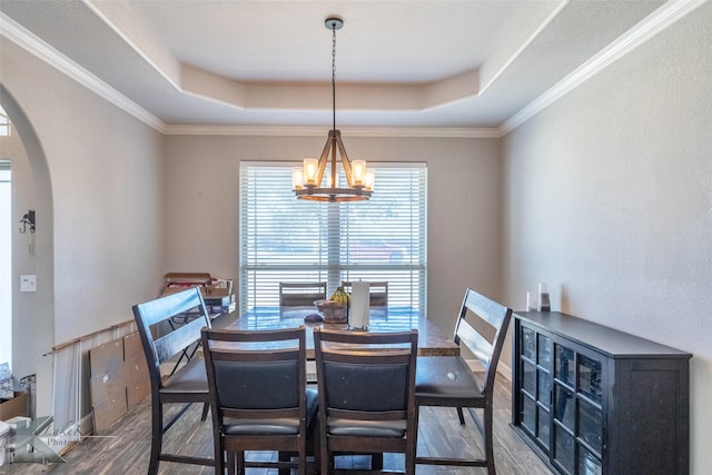 dining area featuring arched walkways, a tray ceiling, and wood finished floors