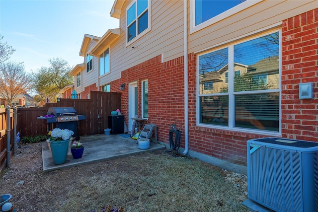 view of property exterior featuring a patio area, a fenced backyard, central AC, and brick siding