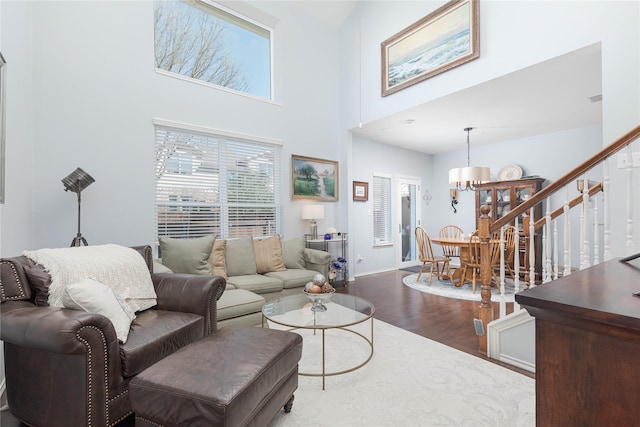 living room featuring baseboards, a towering ceiling, wood finished floors, stairs, and a chandelier