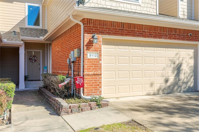 entrance to property featuring a garage, roof with shingles, concrete driveway, and brick siding