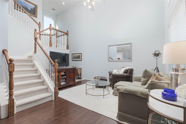 living area with dark wood-style floors, stairway, a towering ceiling, and a ceiling fan