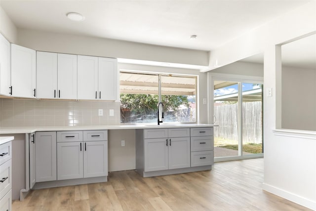 kitchen with light countertops, gray cabinets, a sink, and decorative backsplash