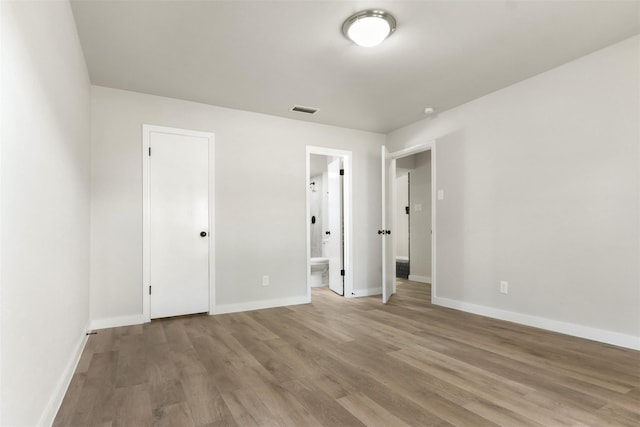 unfurnished bedroom featuring ensuite bath, wood finished floors, visible vents, and baseboards