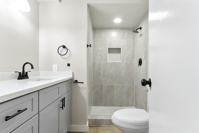 bathroom with toilet, tiled shower, and vanity