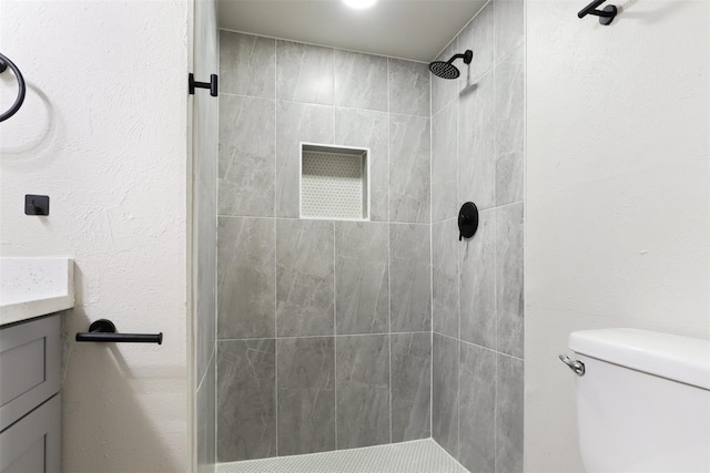 bathroom with toilet, a textured wall, a tile shower, and vanity