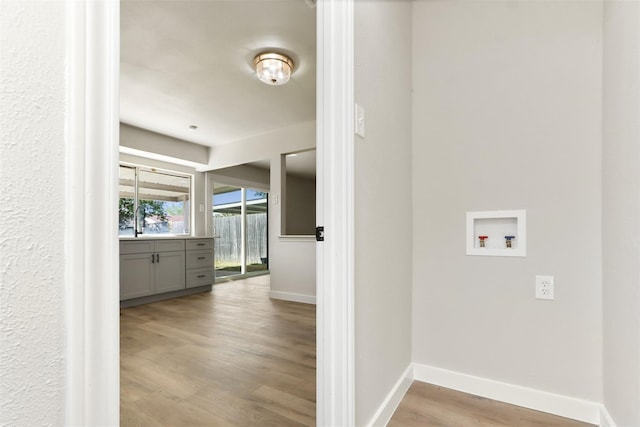 clothes washing area with hookup for a washing machine, light wood-style floors, a sink, laundry area, and baseboards