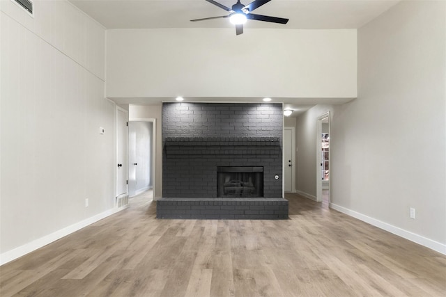 unfurnished living room with baseboards, visible vents, a ceiling fan, light wood-style floors, and a brick fireplace