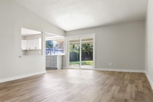 spare room featuring light wood finished floors, baseboards, vaulted ceiling, and a sink