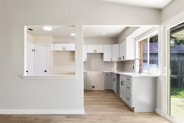 kitchen with tasteful backsplash, light countertops, white cabinetry, a sink, and light wood-type flooring