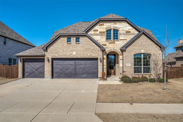 french provincial home featuring concrete driveway, brick siding, an attached garage, and roof with shingles