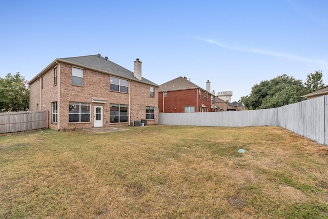 rear view of property with brick siding, a lawn, a chimney, and a fenced backyard