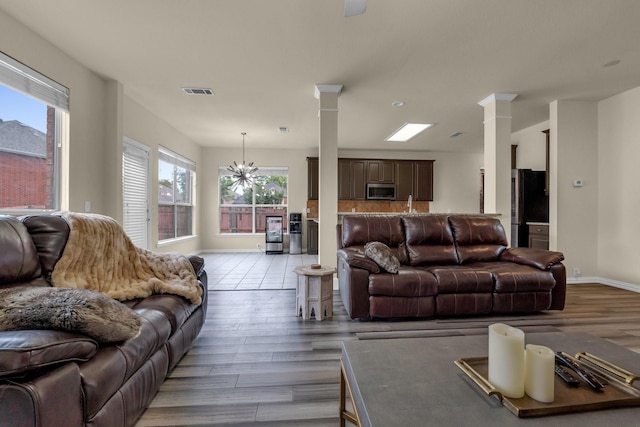 living area with visible vents, light wood-type flooring, decorative columns, and a notable chandelier