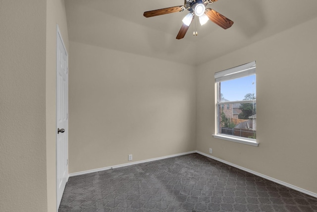 empty room featuring dark colored carpet, a ceiling fan, and baseboards