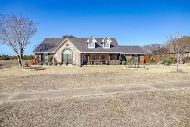 new england style home with a front yard, covered porch, brick siding, and roof with shingles