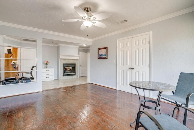 interior space featuring a textured wall, wood finished floors, visible vents, ornamental molding, and a tiled fireplace