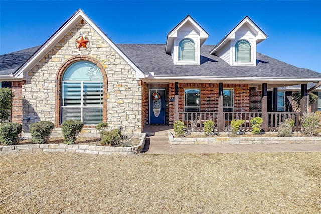 view of front of property featuring roof with shingles, a front yard, a porch, and brick siding