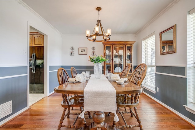 dining area featuring a chandelier, visible vents, crown molding, and light wood finished floors