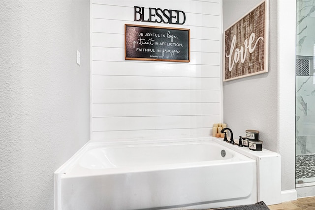 bathroom with a bath, a textured wall, and walk in shower