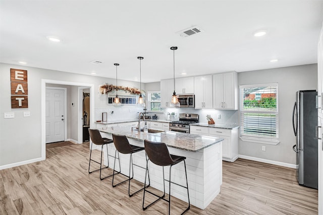 kitchen featuring a kitchen bar, visible vents, a sink, tasteful backsplash, and stainless steel appliances