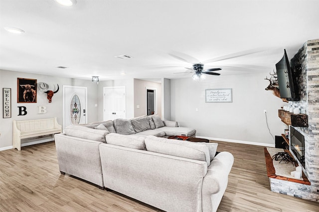 living area featuring a ceiling fan, visible vents, baseboards, a fireplace, and light wood-style floors