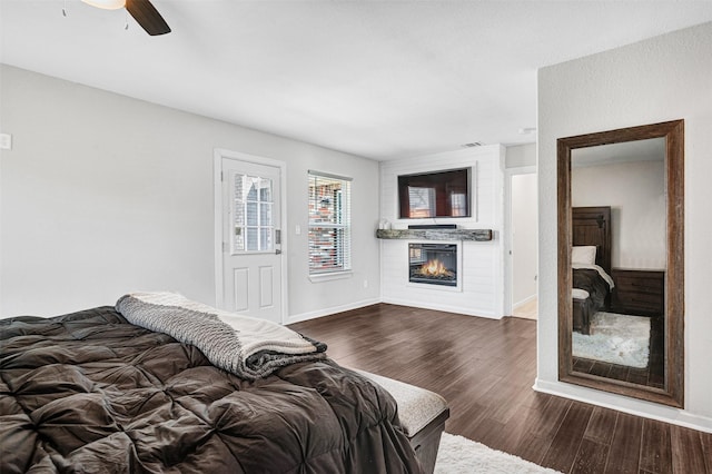 bedroom with visible vents, dark wood-type flooring, a ceiling fan, a glass covered fireplace, and baseboards