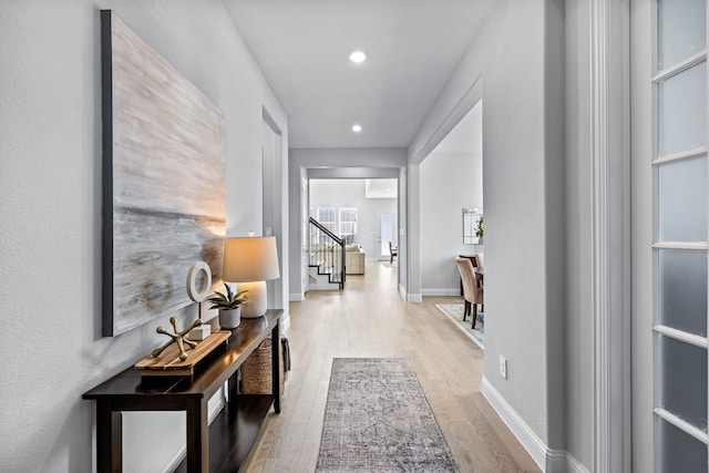 corridor featuring light wood-style flooring, stairs, baseboards, and recessed lighting