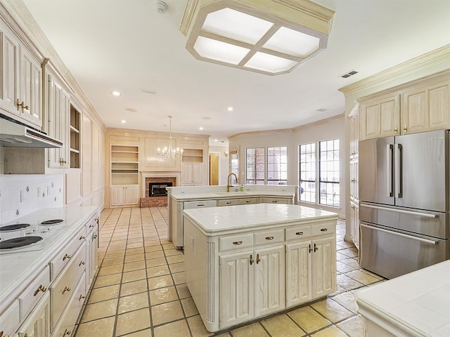 kitchen featuring freestanding refrigerator, light countertops, a center island with sink, and decorative light fixtures