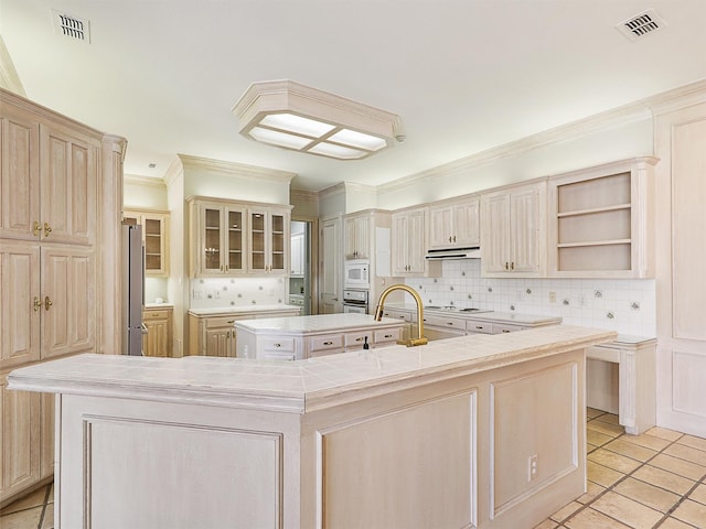 kitchen featuring white appliances, visible vents, light countertops, a center island with sink, and glass insert cabinets