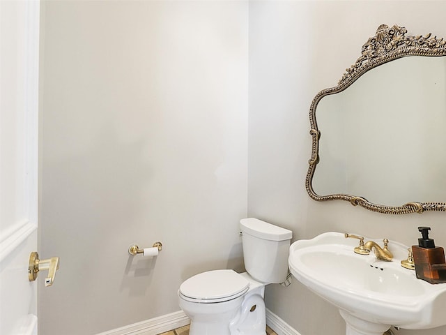 half bathroom featuring toilet, baseboards, and a sink