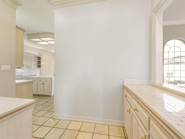 kitchen with light tile patterned floors, tasteful backsplash, tile counters, ornamental molding, and cream cabinets