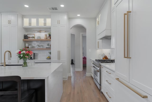 kitchen featuring light stone counters, open shelves, visible vents, white cabinets, and high end stove