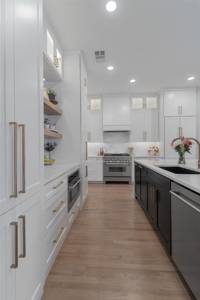 kitchen with glass insert cabinets, appliances with stainless steel finishes, white cabinetry, open shelves, and a sink