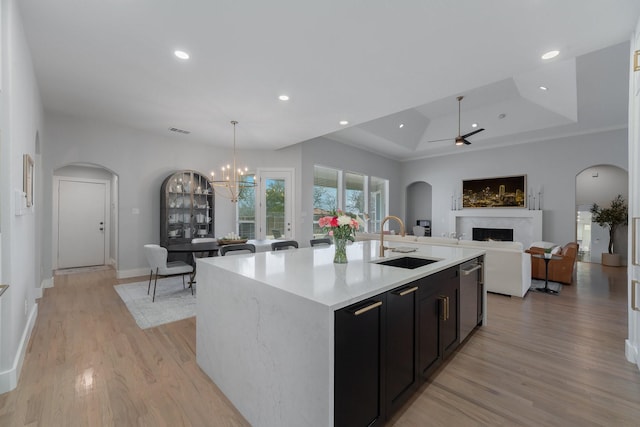 kitchen with arched walkways, a sink, open floor plan, light countertops, and an island with sink