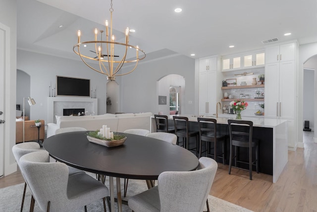 dining area featuring arched walkways, light wood finished floors, recessed lighting, visible vents, and a premium fireplace