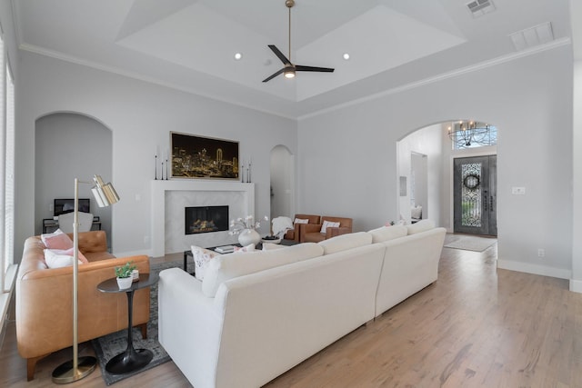 living area with light wood-style flooring, a premium fireplace, visible vents, ornamental molding, and a tray ceiling