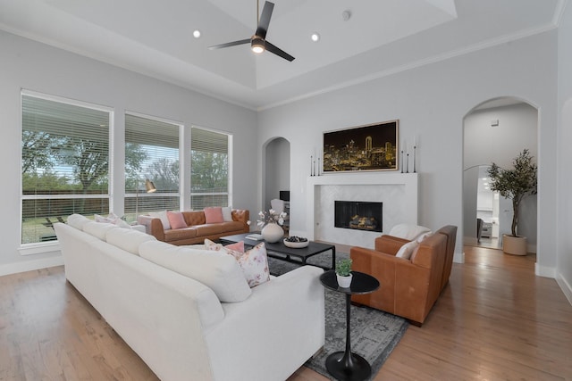 living room featuring a fireplace, arched walkways, a raised ceiling, and a wealth of natural light