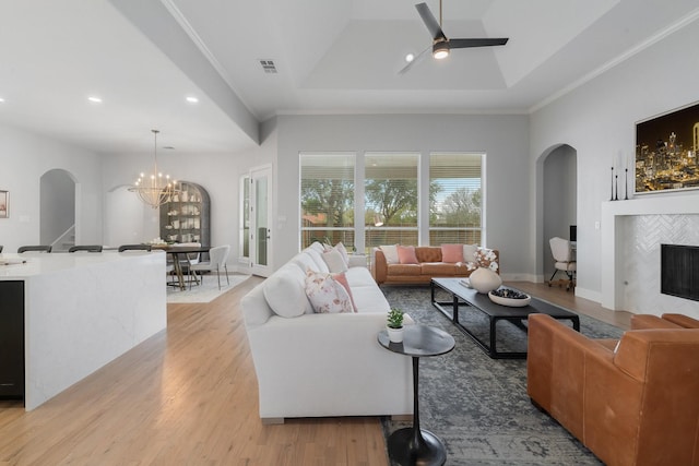 living area with ceiling fan with notable chandelier, a fireplace, visible vents, light wood finished floors, and a raised ceiling