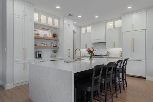 kitchen with a kitchen island with sink, open shelves, white cabinets, and custom range hood