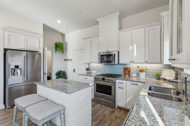 kitchen featuring premium appliances, a kitchen breakfast bar, light stone countertops, white cabinetry, and a sink