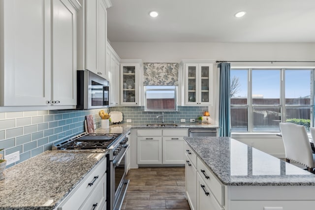 kitchen with glass insert cabinets, a center island, stainless steel appliances, white cabinetry, and a sink