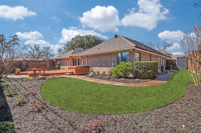 view of side of property featuring brick siding, a yard, a hot tub, and a fenced backyard