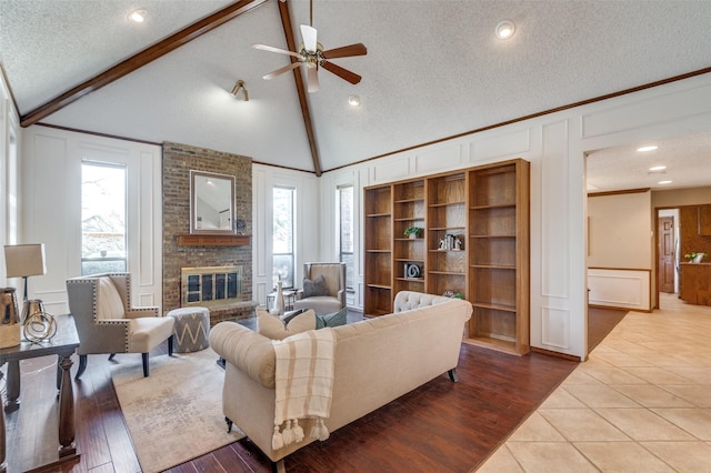 living area featuring vaulted ceiling with beams, a brick fireplace, plenty of natural light, and a decorative wall