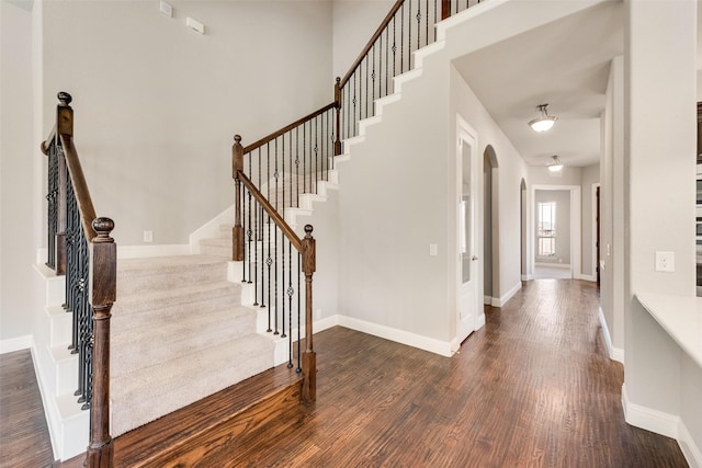 foyer entrance featuring arched walkways, dark wood-style flooring, baseboards, and stairs