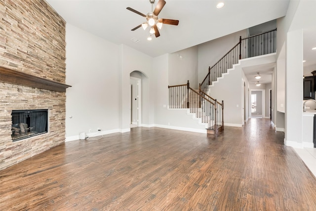 unfurnished living room with a fireplace, dark wood-type flooring, ceiling fan, baseboards, and stairs